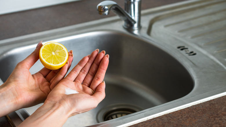 Temizlemeye hazırlanan paslanmaz çelik bir lavabonun üzerinde limon ve tuz tutan kadın