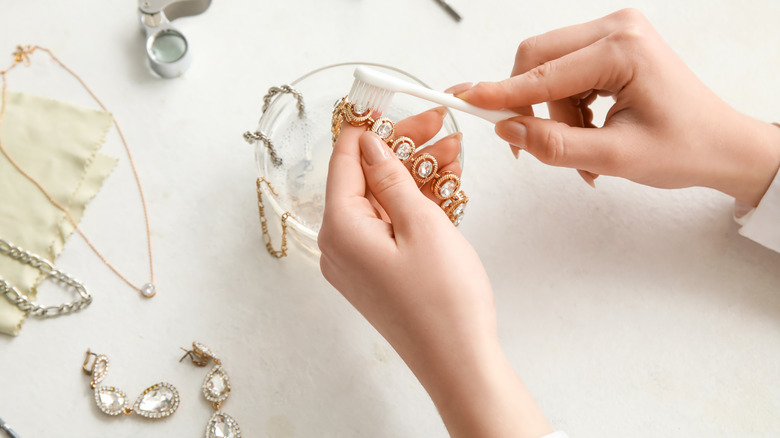 Diş fırçası ile bir cam kasede mücevherleri temizleyen kadın