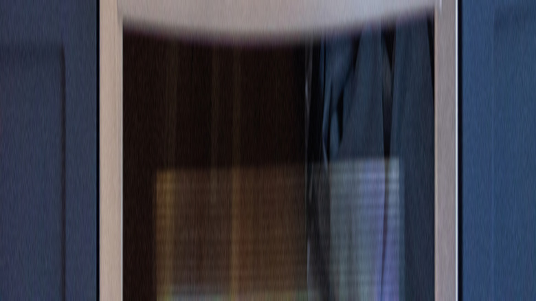 Ön brülörde siyah su ısıtıcısı ve ahşap mutfak eşyaları ve tezgahta mikrodalga fırın ile cam soba üstü