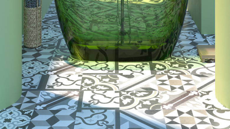 Merkezde şeffaf yeşil küvet, yerde geometrik fayans ve okyanusa bakan yeşil duvarlara sahip bir açık banyo.