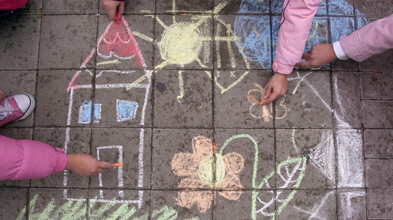 Bir evin, güneşin ve kaldırım tebeşirli çiçeklerin resimlerini çizmek