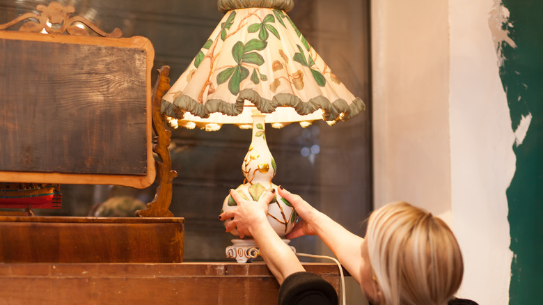 Bir kadın bir raftan eski bir çiçek lambası almak için uzanır.