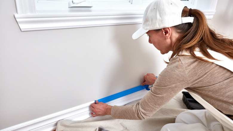 Bir kadın, onları boyamadan önce mavi ressamın bandı ile süpürgelikleri bantlar.