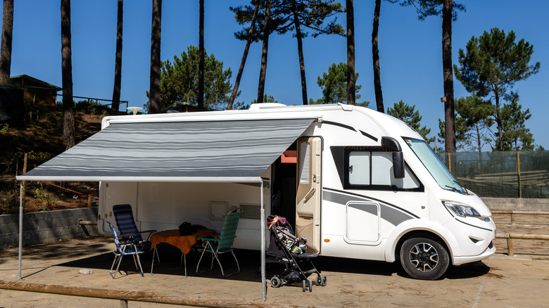 Önünde sandalyeler ve bebek arabası bulunan bir RV parkına park edilmiş bir karavan