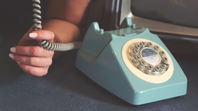 W Manicured Hand, açık mavi döner bir telefonun kablosunu tutar