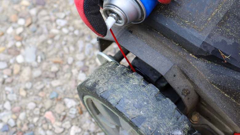 Çim biçme makinesi lastiğine WD-40 püskürtüyor