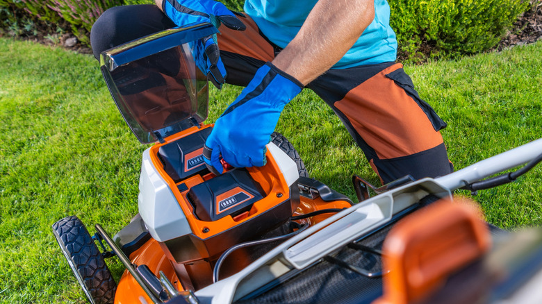 Elektrikli çim biçme makinesindeki pilleri kaldıran kişi
