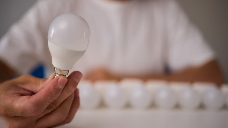 Bulanık bir arka plana sahip bir LED ampulü tutan bir adamın yakından görüntüsü.