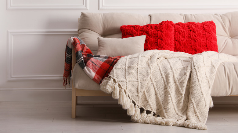 Kırmızı yastık ve tartan ve ahşap battaniye ile bej kanepe.