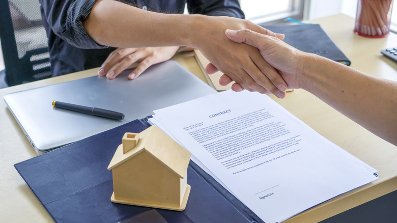 İki kişi gayrimenkul ile ilgili yasal bir belgenin üzerinden el sıkışın