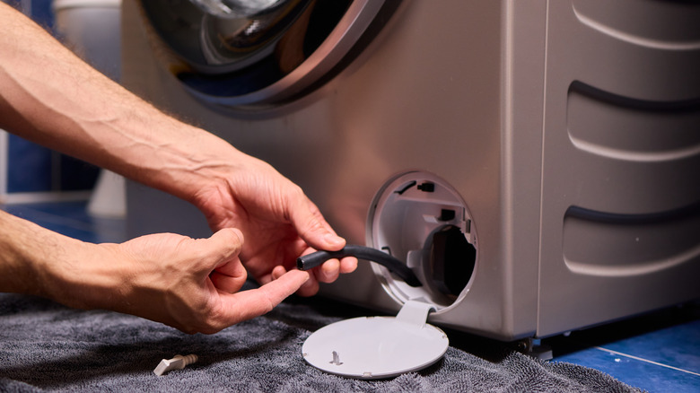 Çamaşır makinesinin drenaj borusunu havlu üzerinde tutan bir adamın ellerinin yakın çekimi