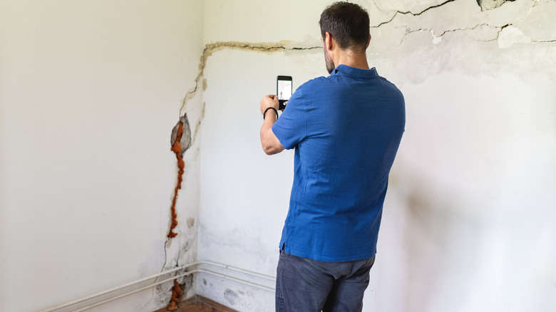 Hasarlı bir duvarın yanında durup fotoğraf çeken kişi