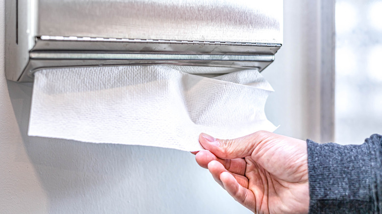 Birisi banyoya monte edilmiş dağıtıcıdan kağıt havlu çekiyor