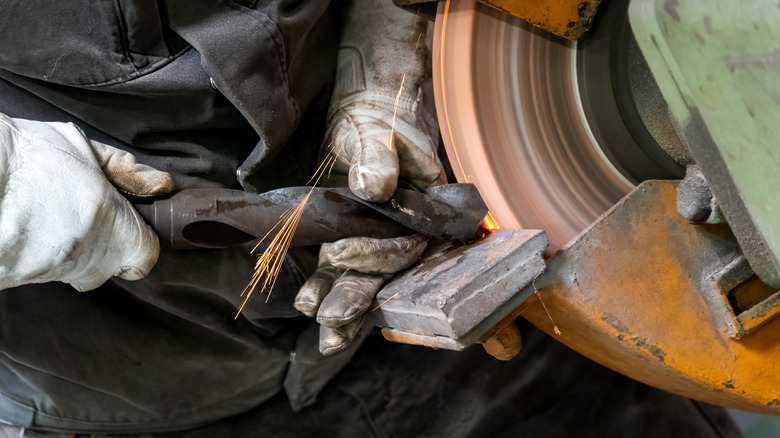 Eldivenli elleri olan bir kişi tezgah taşlayıcı kullanarak matkap ucunu keskinleştiriyor