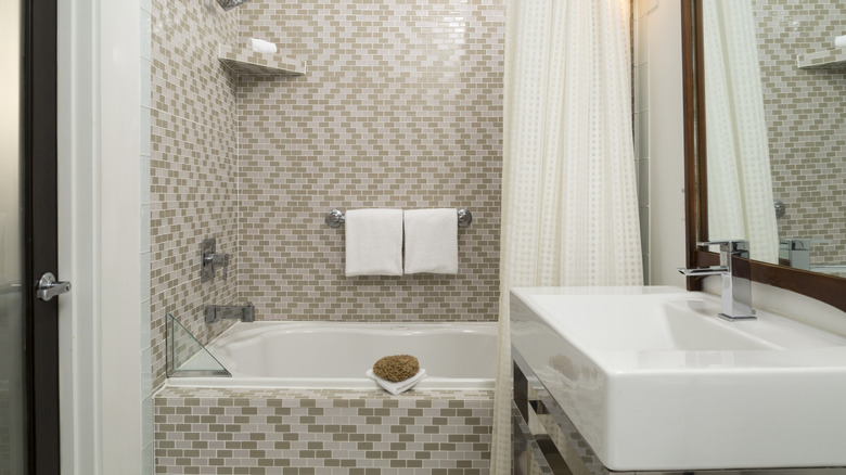 Bir girintili küvet, beyaz ve bej çinilerden oluşan bir desenle dekore edilmiştir.