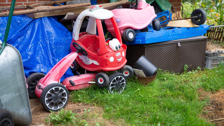 Bir evin yan tarafındaki Little Tikes arabası ve diğer çocuk araçlarının da dahil olduğu çimenlik dağınıklığı