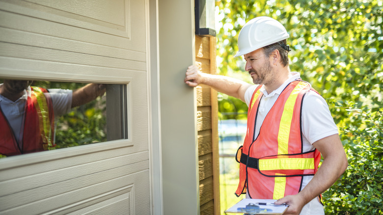 Turuncu hi-vis yelekli adam garaj kapısını inceliyor