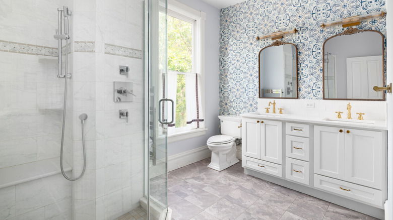 Duşakabin, beyaz dolaplar, ikili lavabo ve aynalar ile desenli mavi-beyaz duvar kağıdı içeren modern bir banyo