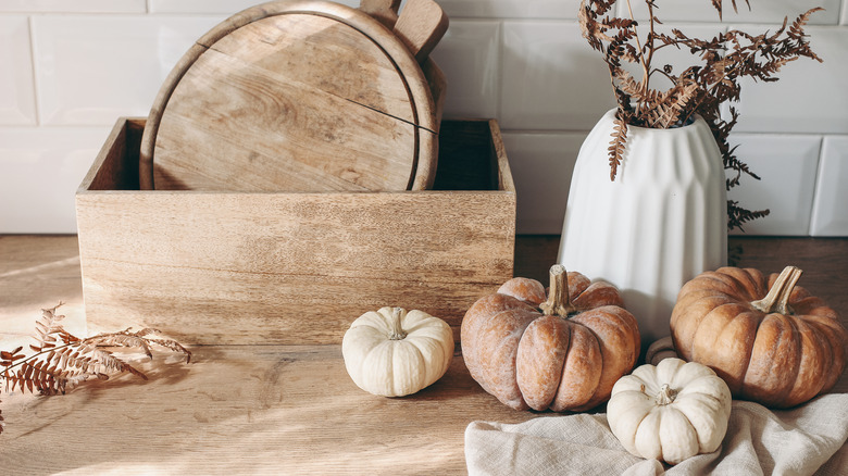 Mutfaktaki ahşap kutunun önünde bir vazoda yumuşak renklerde balkabakları ve kurutulmuş bitkiler