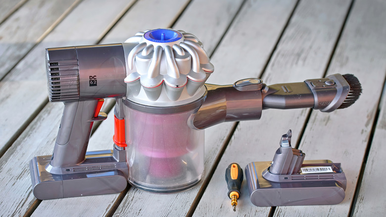 Elde taşınan Dyson elektrikli süpürge, tornavida ve yedek pil, ahşap bir güverte üzerinde duruyor