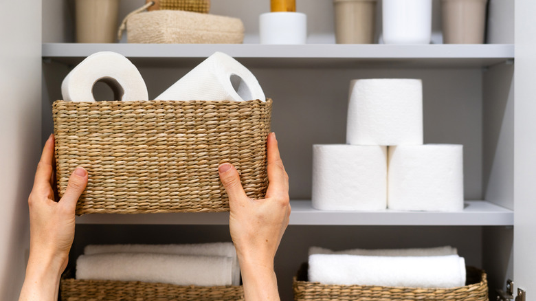Tuvalet kağıdıyla dolu hasır sepeti rafa koyan bir kadın