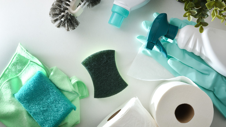 yeşil temizleyiciler, tuvalet kağıdı ve beyaz bir yüzey üzerinde duran bir sprey şişesi.