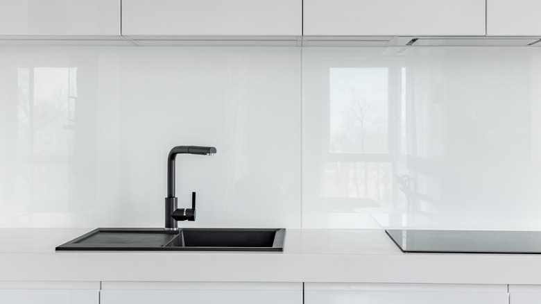 Siyah lavabosu, musluğu ve cam backsplash'ı olan beyaz bir mutfak