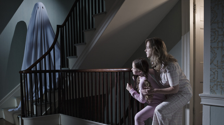 Köşeden merdivenlerdeki hayalete bakan bir anne ve kızı.