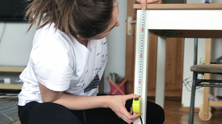 Bir masanın yüksekliğini ölçen bir kadın