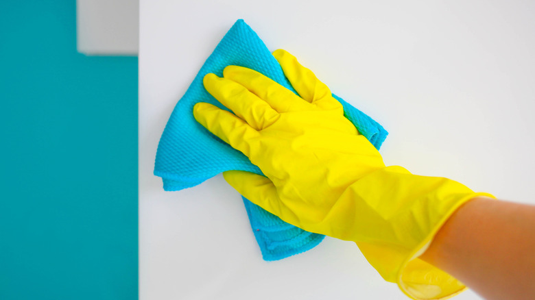 Eldiven giyen bir kişi turkuaz bir bezle duvarı temizliyor