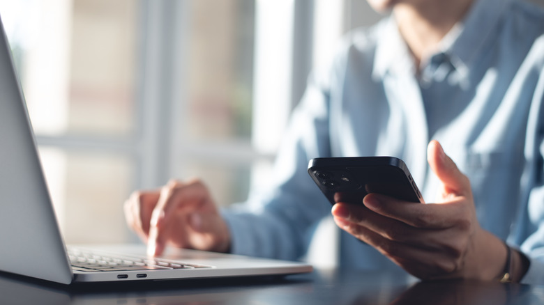 Bir kişi evde dizüstü bilgisayarını ve cep telefonunu kullanıyor