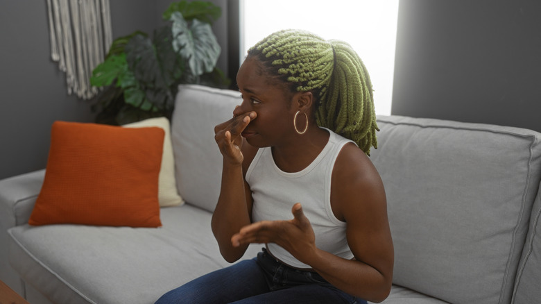 Kanepede oturan bir kadın, kötü kokuya tepki olarak burnunu tutuyor.