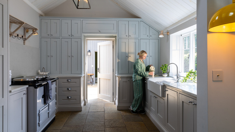 açık mavi tavandan tabana dolaplarla mutfakta duran kadın