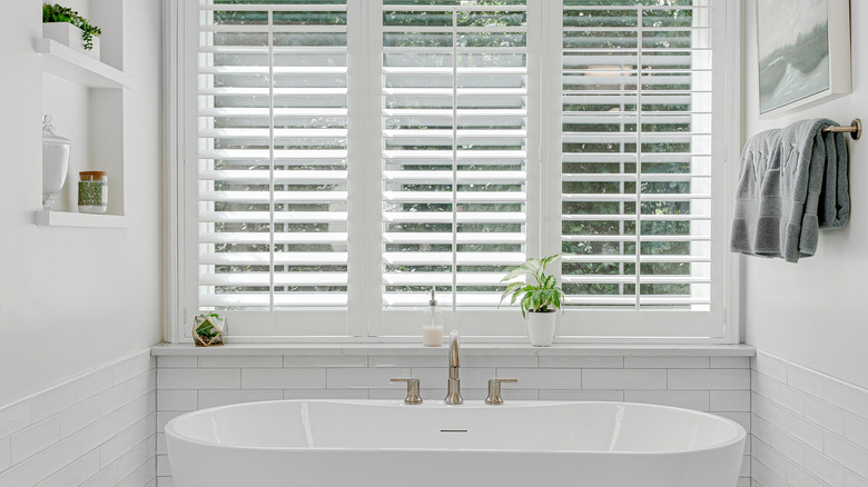 Plantasyon panjurlarıyla sahnelenen, pirinç musluklu iç tasarıma sahip modern lüks derin küvet.