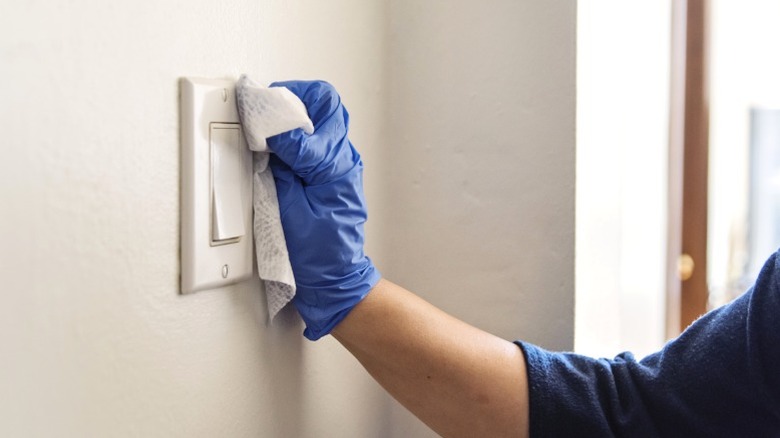 Mutfak ışık anahtarını temizlik mendiliyle temizleyen kişi