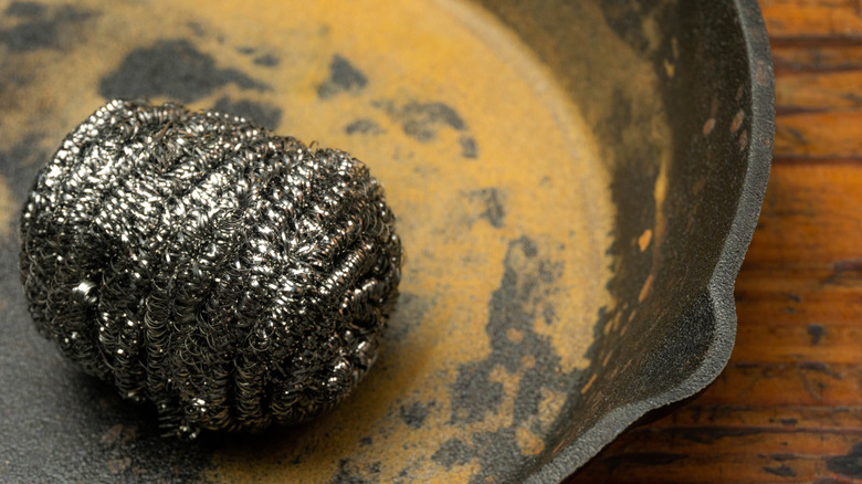 Paslı bir dökme demir tava üzerinde çelik yün yıkayıcı.