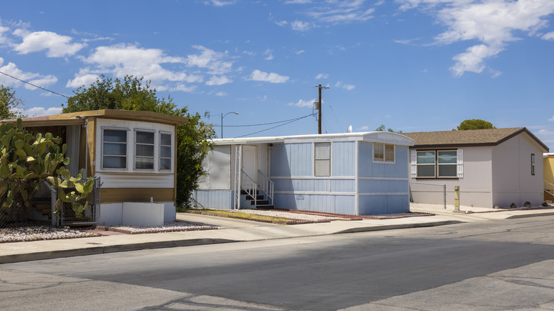 Küçük bulutlarla güneşli gökyüzünün altında bir sokakta üç mobil ev.