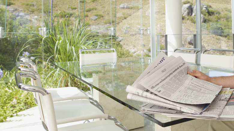 Temiz bir pencere duvarının önünde bir deste gazete tutan bir el.