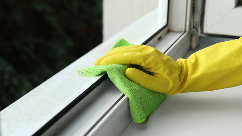 Sarı eldivenli bir el metal pencere çerçevesini yeşil bir bezle temizliyor.