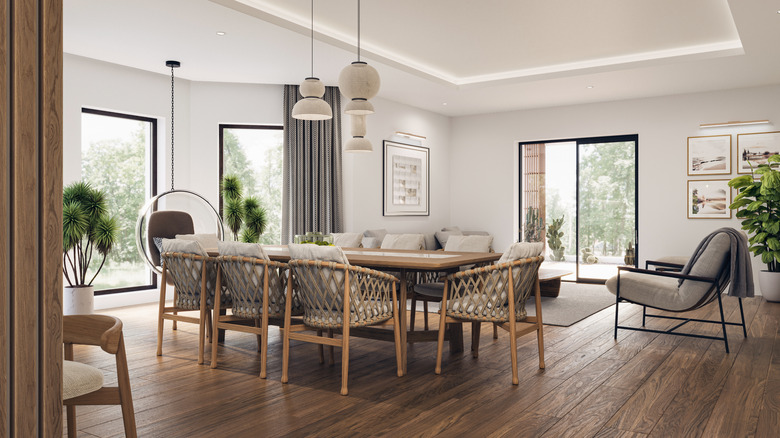 Büyük pencereler, TV duvarı, gri kanepe, yemek masası ve parke zeminli açık alan oturma odası ve mutfak iç mekanı.