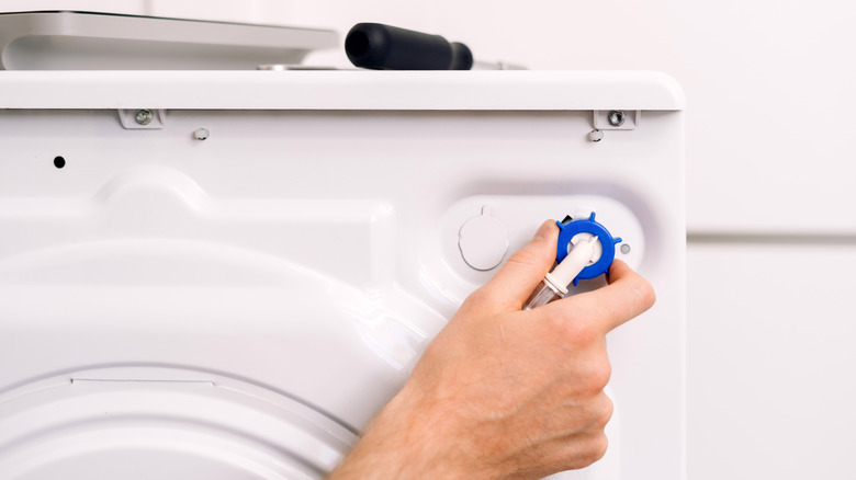 Bir kişinin eli çamaşır makinesinin arkasındaki hortumu sıkıyor