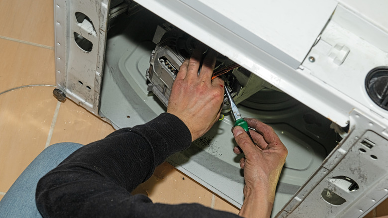 Bir kişinin elleri çamaşır makinesinin arkasını tamir ediyor