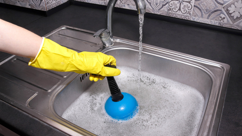 Sarı lastik küreli kişi tıkalı lavaboya dalıyor