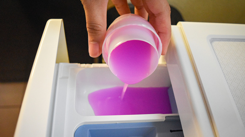 çamaşır makinesine pembe çamaşır yumuşatıcısı döken kişi