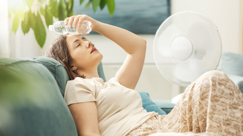 Alnına su şişesini dayayan genç bir kadın vantilatörün önünde oturuyor.