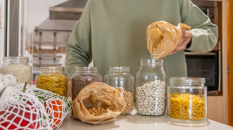 Kuru malzemeleri cam saklama kaplarına döken bir kişi