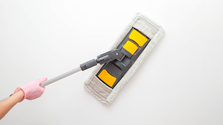 Pembe eldivenli el beyaz duvarı beyaz ve sarı paspasla yıkıyor.