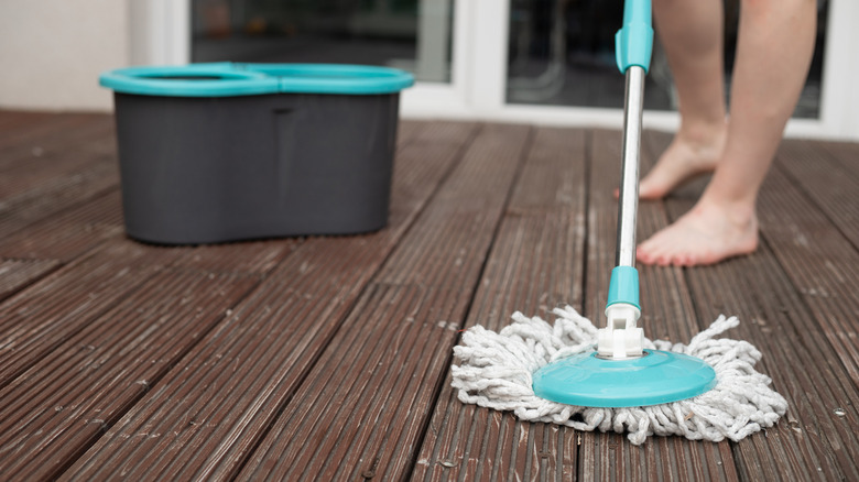 Bir ev sahibi ahşap güverteyi paspasla yıkıyor.