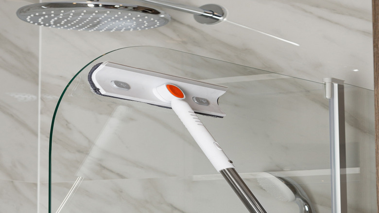 Duş kabininin cam duvarlarını temizlemek için paspas kullanmak.