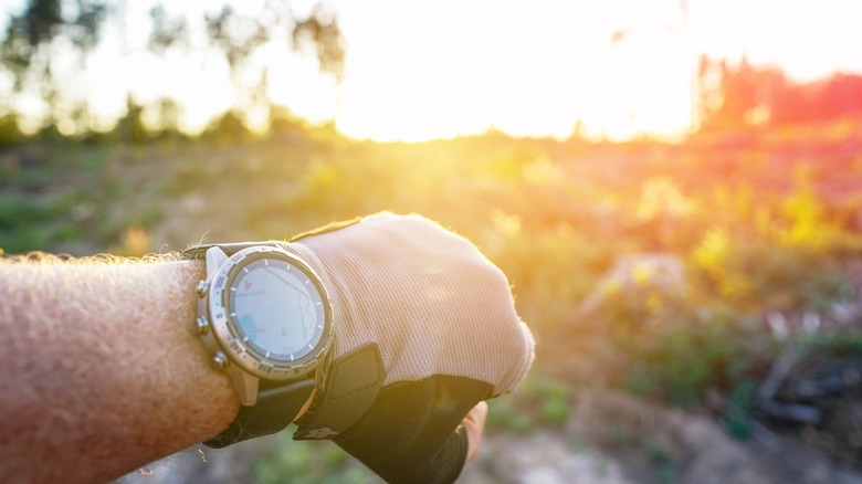 Güneş gökyüzünde batarken bir kişi saatini kontrol ediyor